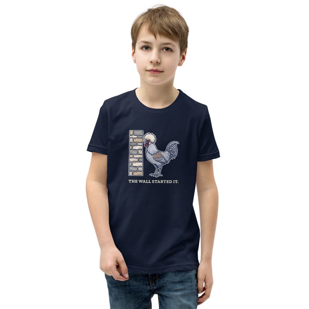 Kids t-shirt with a cartoon of a small crested rooster crowing at a stone wall and the words The Wall Started It. Shown in Navy.